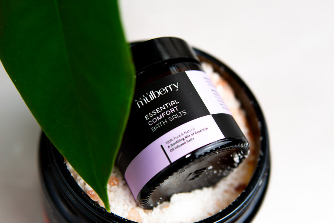 Small jar of white and pink bath salts nestling in a large jar with leaf partially over view